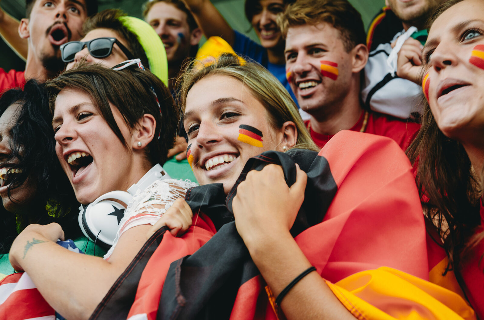 Jubelnde Fußballfans mit Deutschland-Flaggen und geschminkten Gesichtern im Stadion