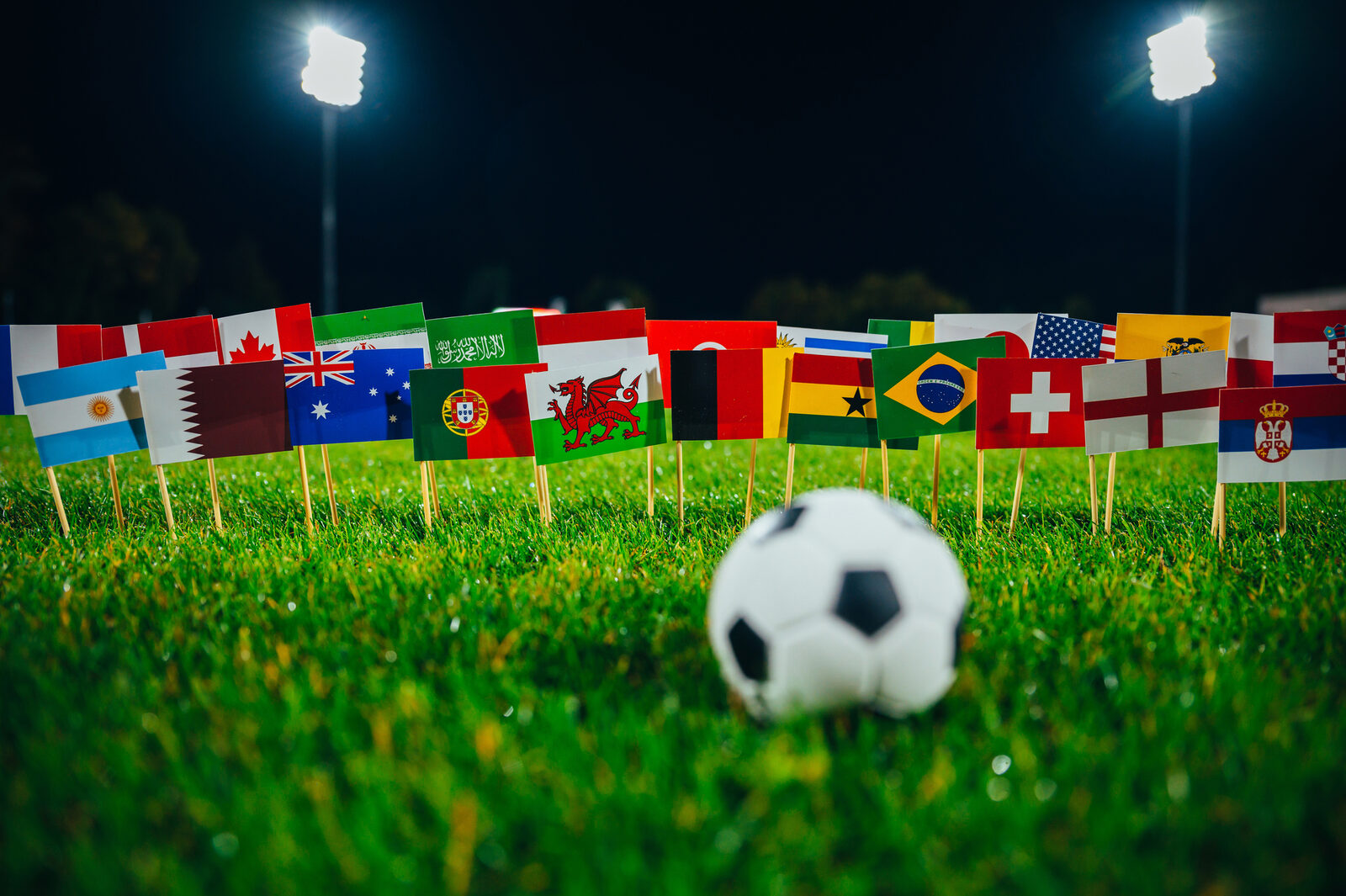 Fußball im Stadion bei Flutlicht, umgeben von Nationalflaggen der WM-2026-Teilnehmer